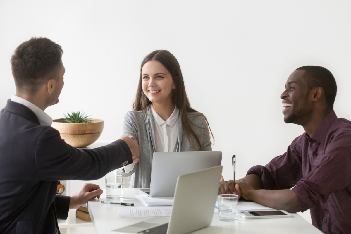 smiling-businesswoman-shaking-hand-male-partner-group-meeting